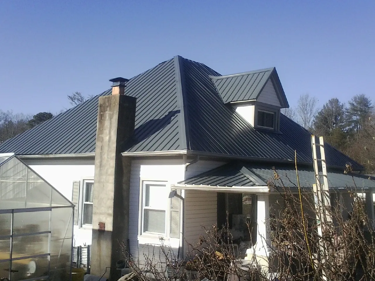 Dark blue standing seam metal roof on a white farmhouse with dormer — Slate & Tile Roof Repair by Roofing Brothers in Verona Beach