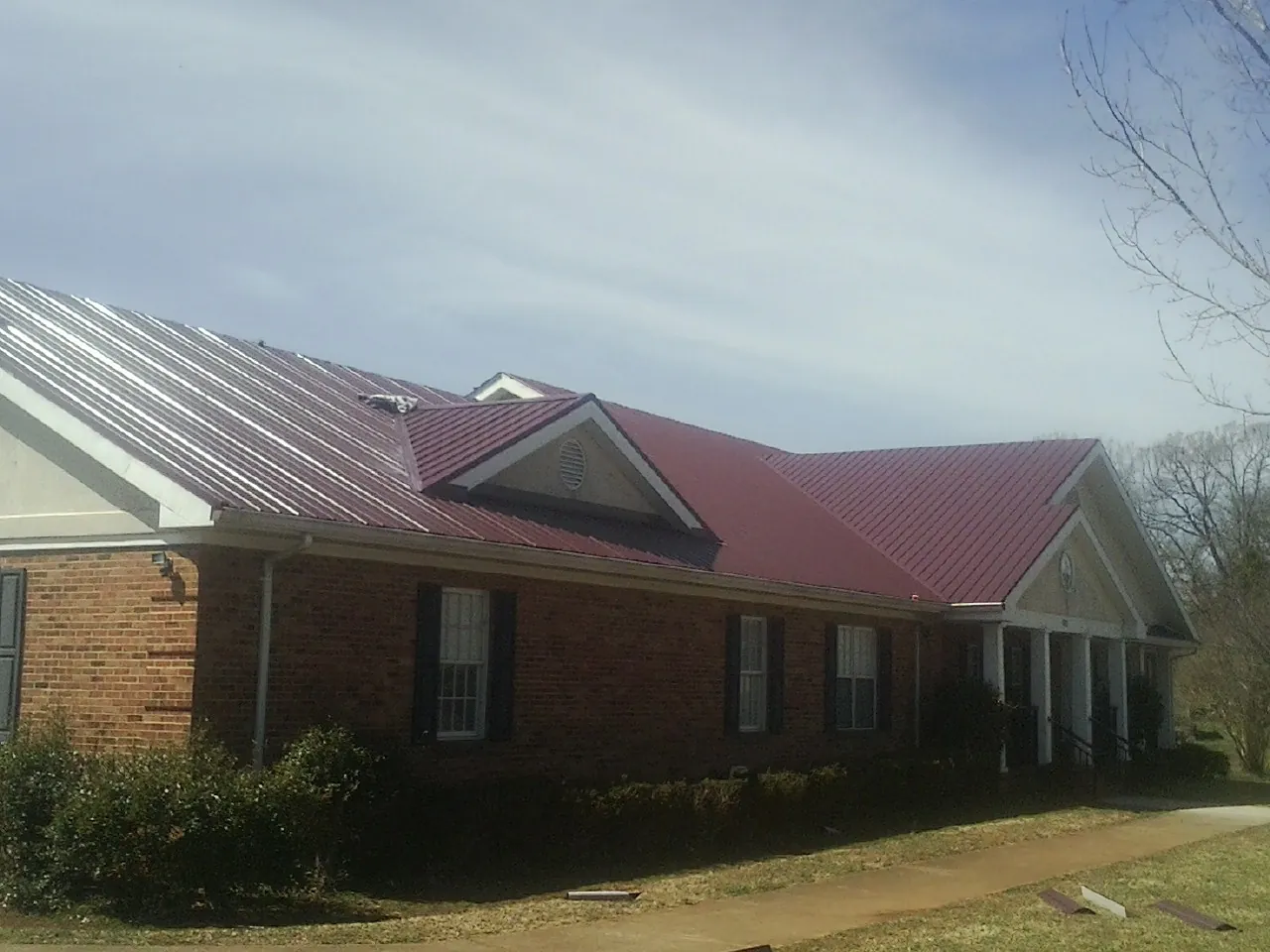 Red metal roof with gabled entries on a long brick building, from a Hail Damage Roof Repair job in Verona Beach