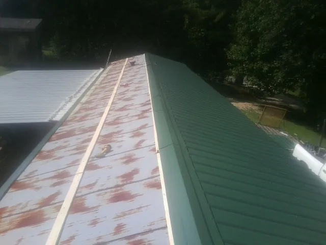 Old rusted panels beside newly installed green metal roofing — Wind Damage Roof Repair by Roofing Brothers in Verona Beach