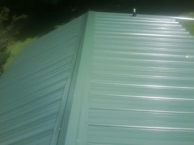 New green metal panels meeting at the ridge of a roof — Flat Roof Repair work by our crew in Verona Beach