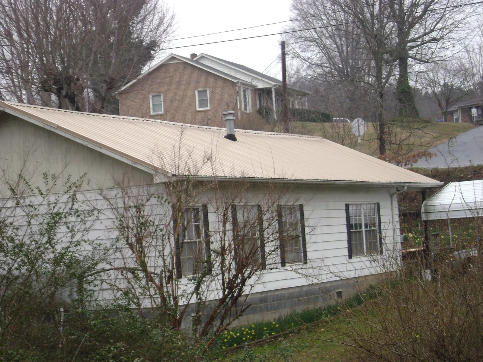 Tan metal roof on a white sided house set into a hillside — Commercial Roofing by Roofing Brothers in Verona Beach
