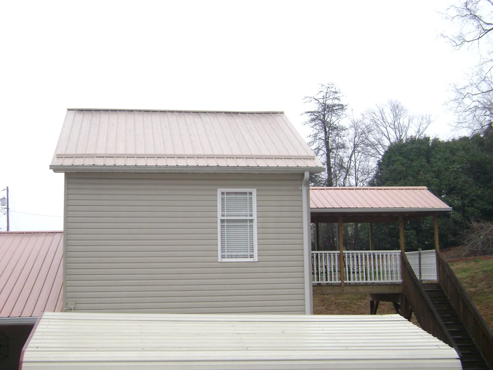 Tan metal roofs on a two story addition and attached porch, from a Roof Replacement job in Verona Beach